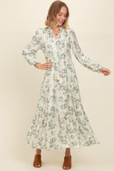 woman wearing a long sleeve floral maxi dress in white and green with a tiered design and tassel details