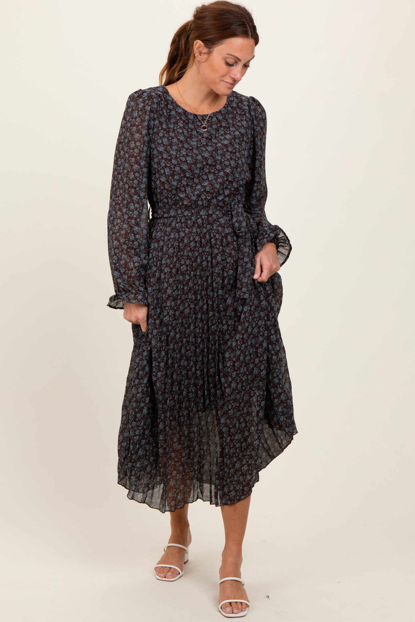 woman wearing a black floral midi dress with long sleeves and a belted waist, standing and looking down
