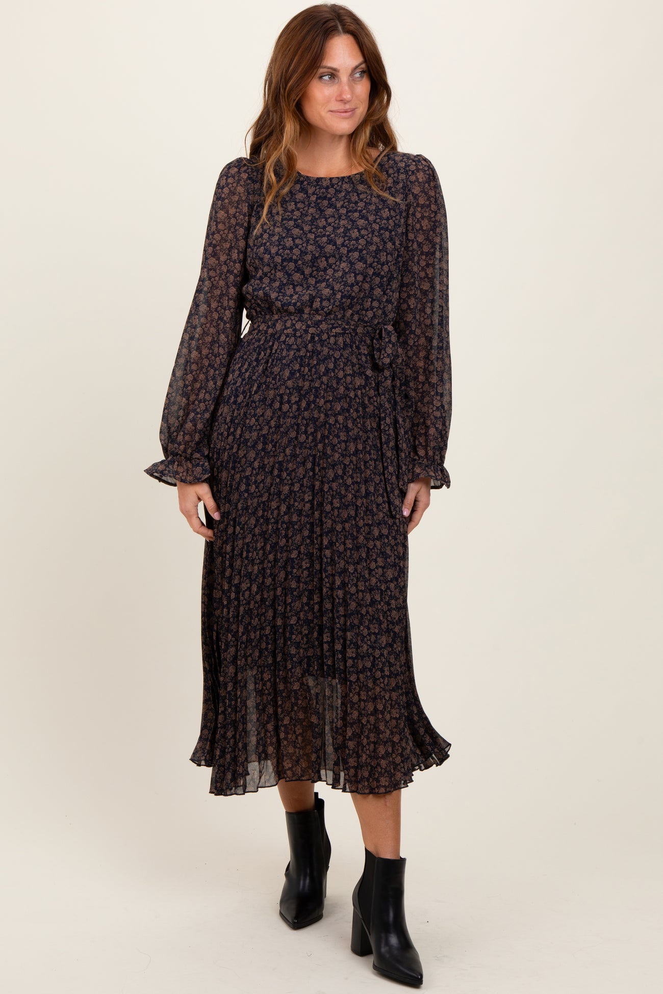 woman wearing a navy floral print midi dress with long sleeves and a tie waist, paired with black ankle boots