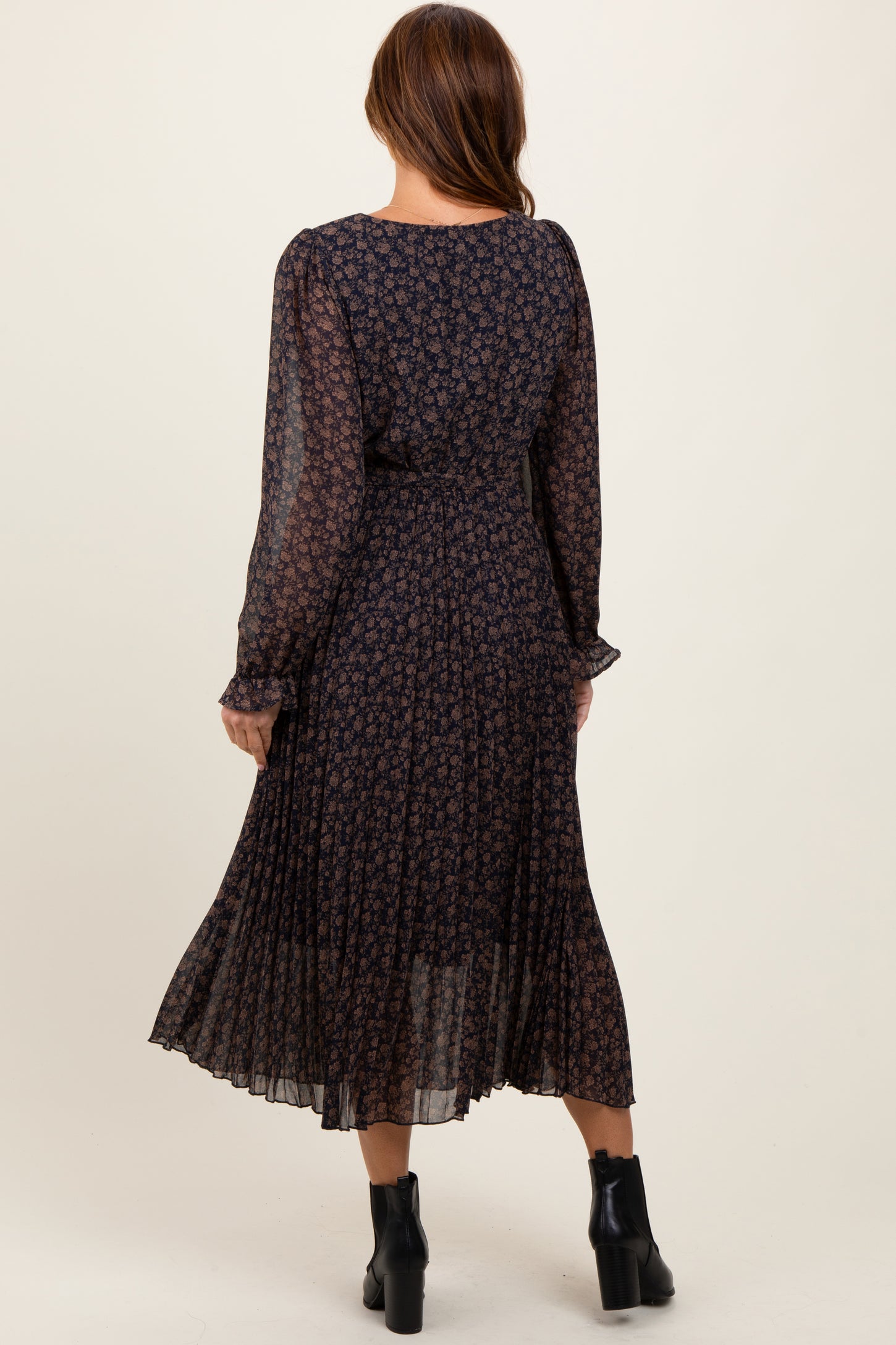 woman wearing a dark floral long sleeve pleated dress, view from the back with ankle boots