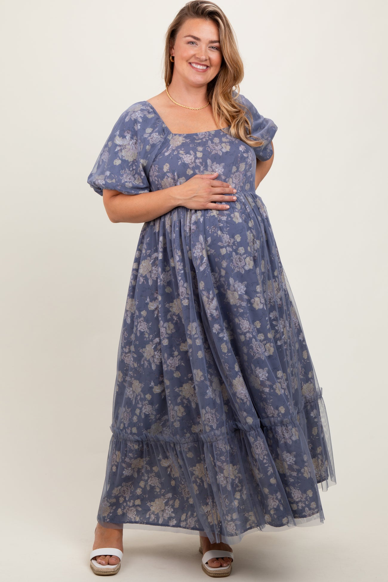 woman wearing a blue floral maternity maxi dress with short puff sleeves and holding her baby bump