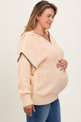 woman wearing a peach knitted maternity sweater with a hood, showing her baby bump, paired with blue jeans