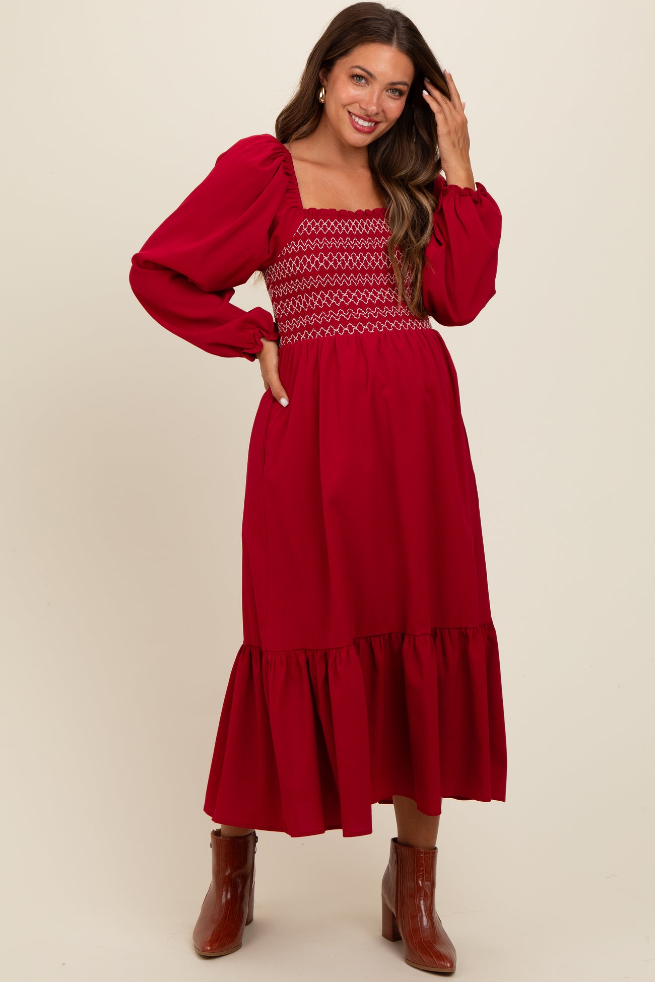 woman wearing a red maternity dress with a smocked bodice and puff sleeves, standing and smiling