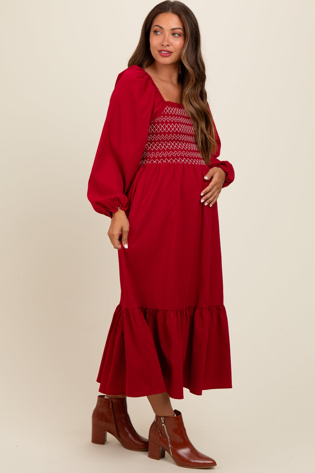 woman wearing a red maternity dress with smocked bodice and ruffle hem, holding her baby bump
