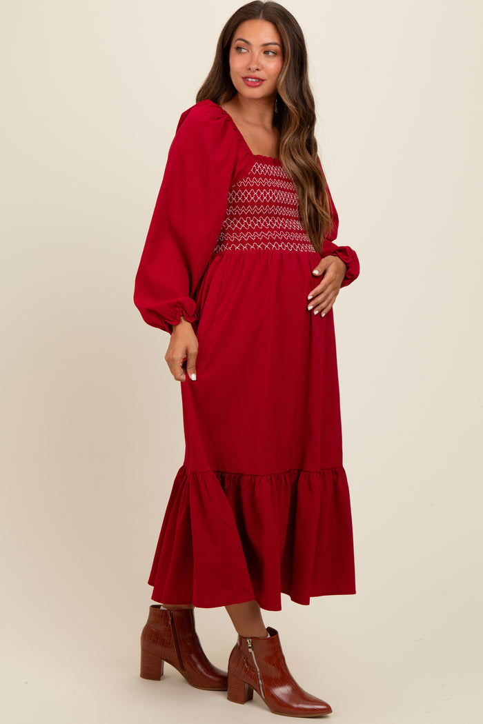 woman wearing a red maternity dress with smocked bodice and ruffle hem, holding her baby bump