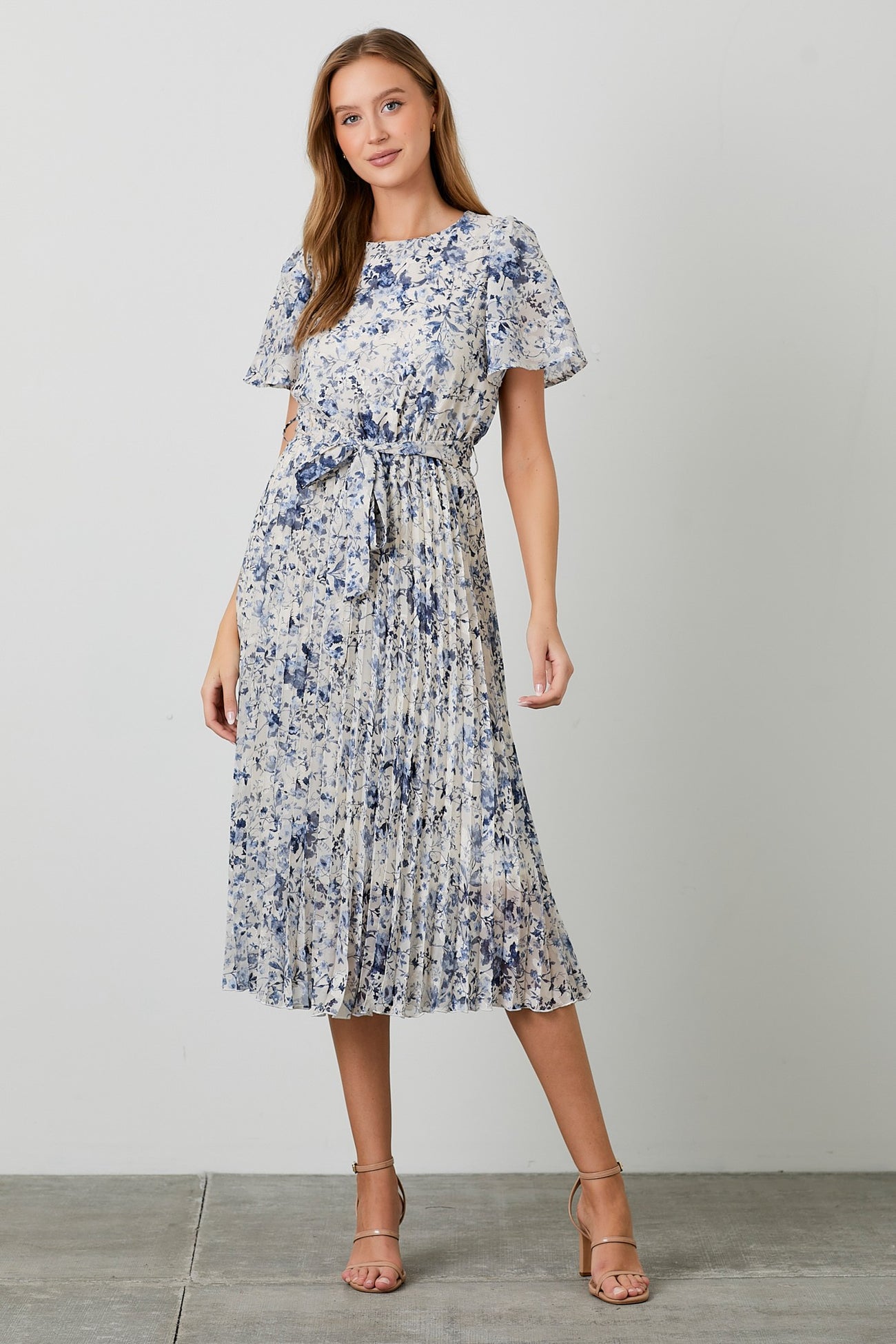 woman wearing a floral pleated midi dress in blue and white with short sleeves and a tie waist