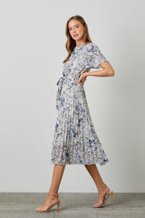 woman wearing a floral pleated midi dress with short sleeves and a tie waist, paired with strappy nude heels