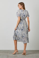 woman wearing a flowy midi dress with a floral print and pleated design, showing a back view with tied detail