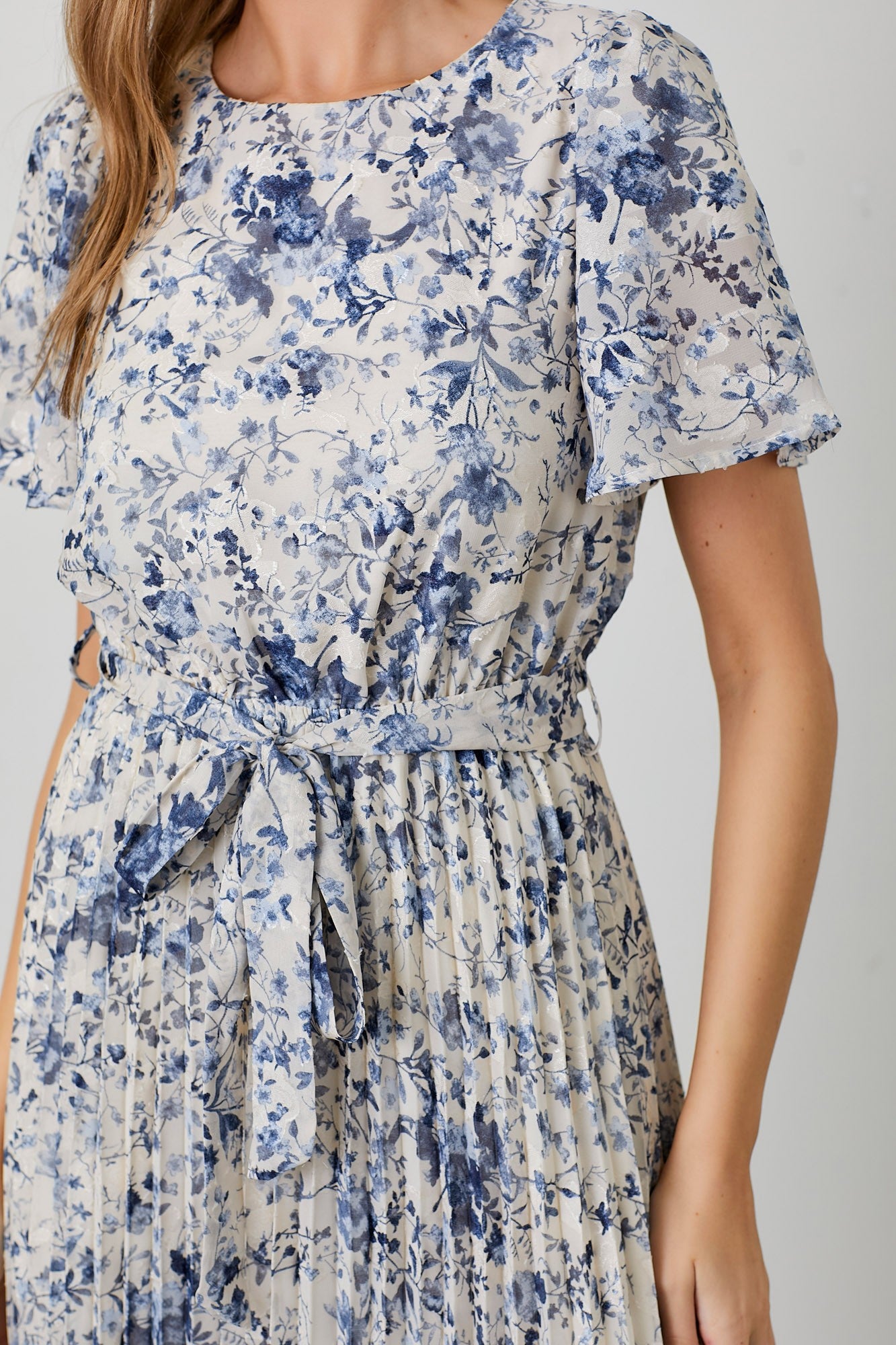 woman wearing a floral patterned dress in shades of blue with short sleeves and a tie waist detail