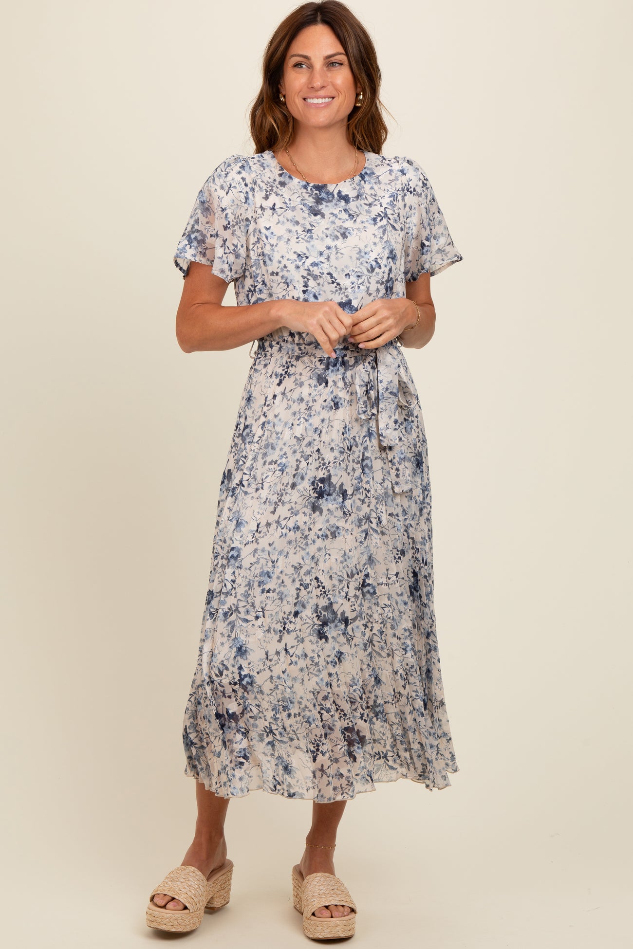 woman wearing a floral print maxi dress in soft blue and cream colors with short sleeves and a tie waist detail
