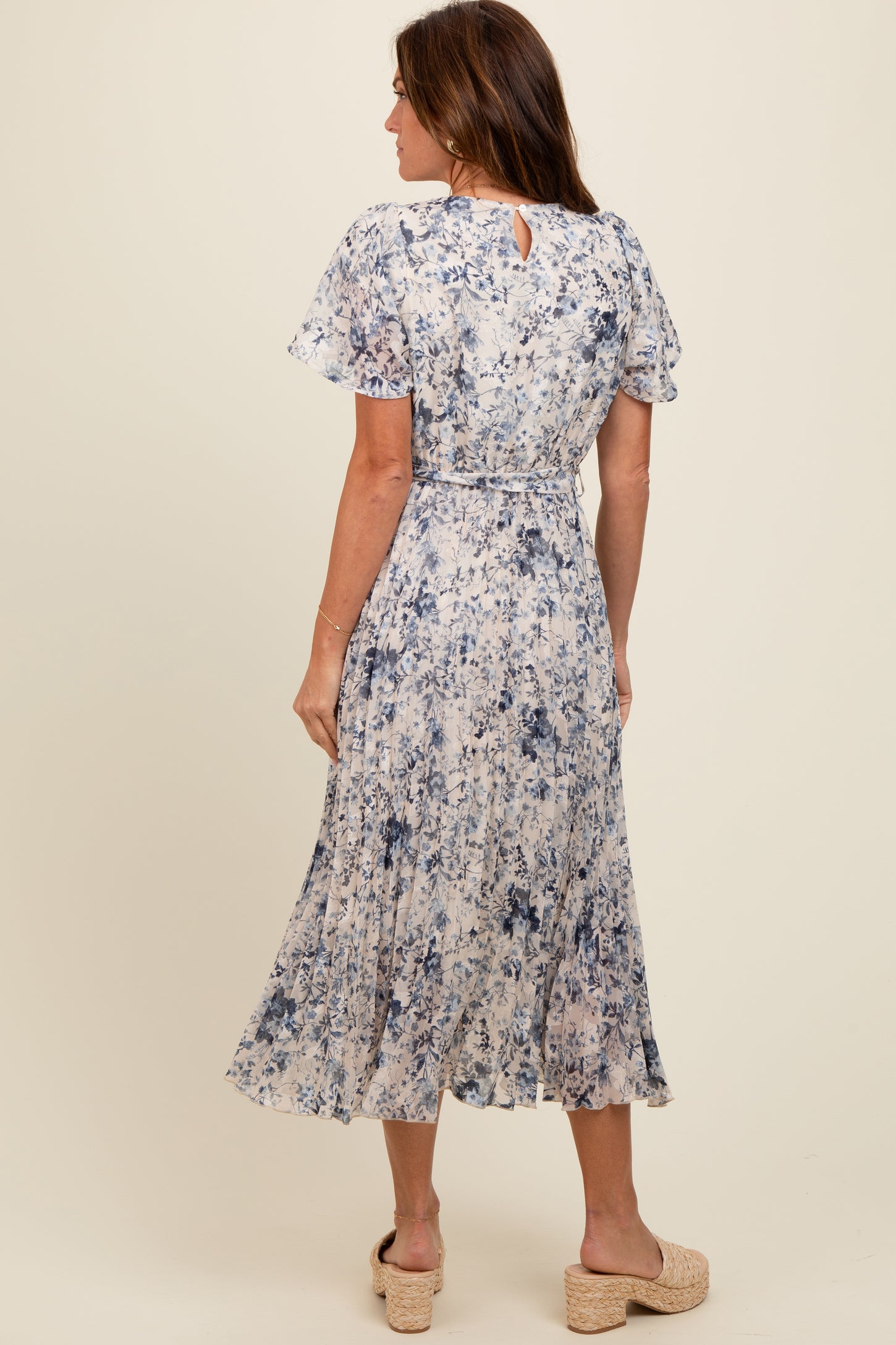 woman wearing a blue and cream floral midi dress with flutter sleeves and keyhole back detail