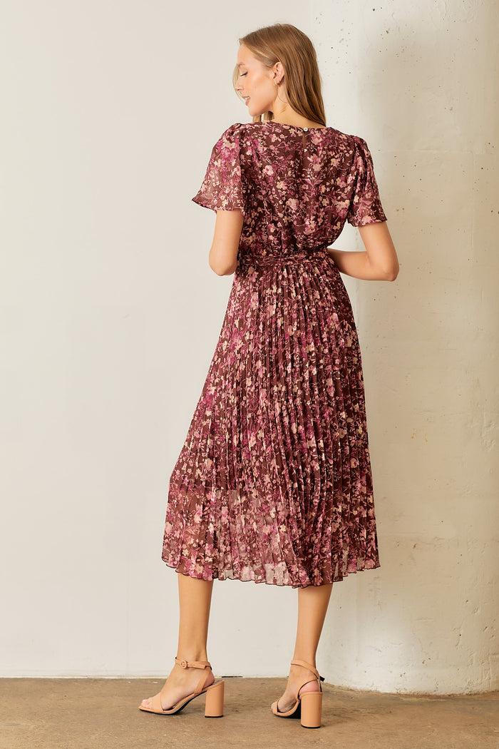 woman wearing a purple floral pleated midi dress, showing the back view with short sleeves and a cinched waist