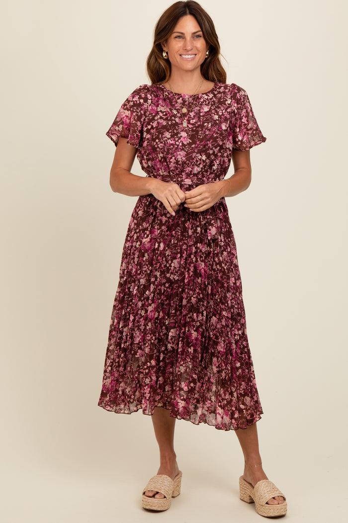 woman wearing a floral midi dress with short sleeves in shades of purple and pink, standing and smiling