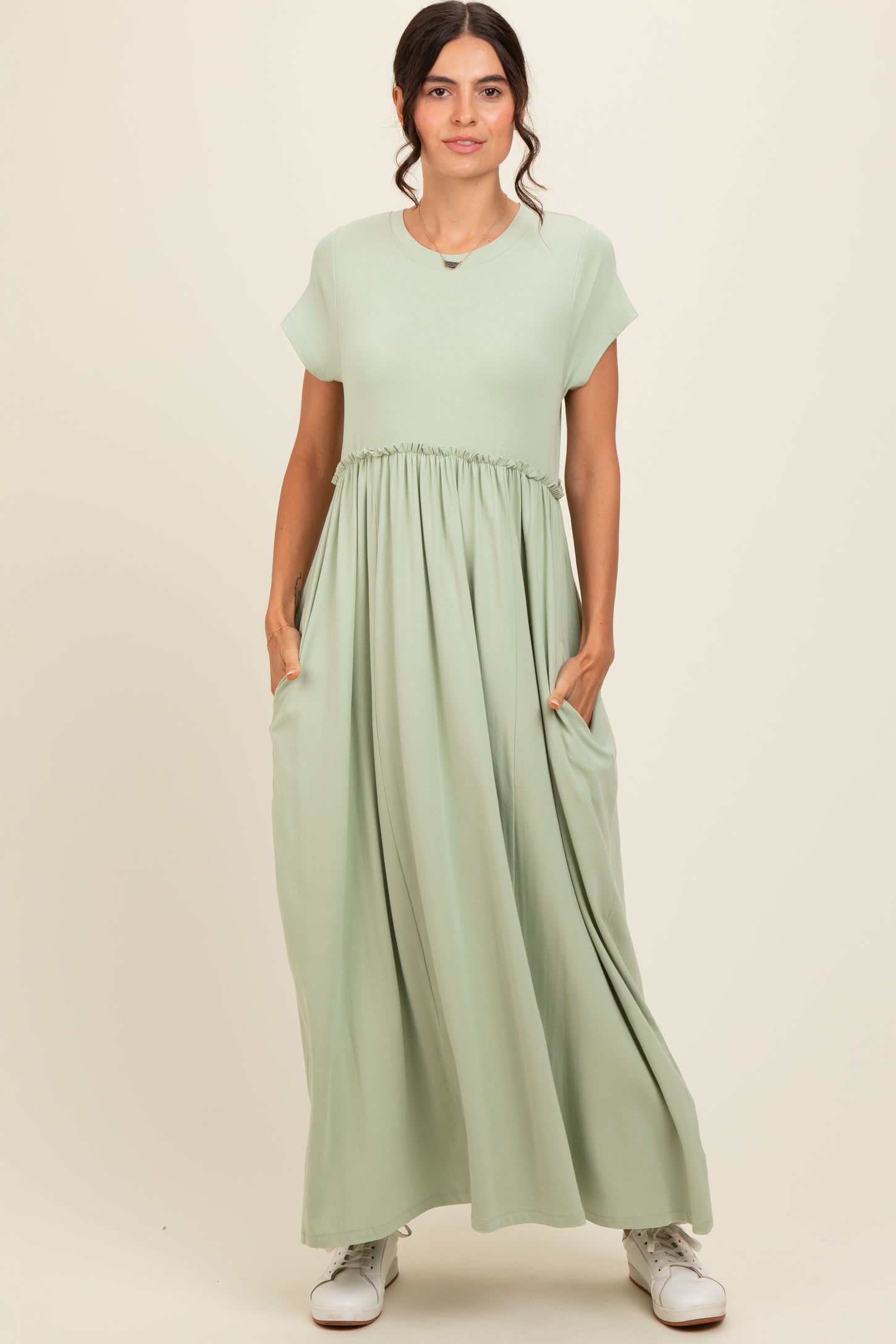 woman wearing a light green maxi dress with short sleeves and a cinched waist, featuring pockets