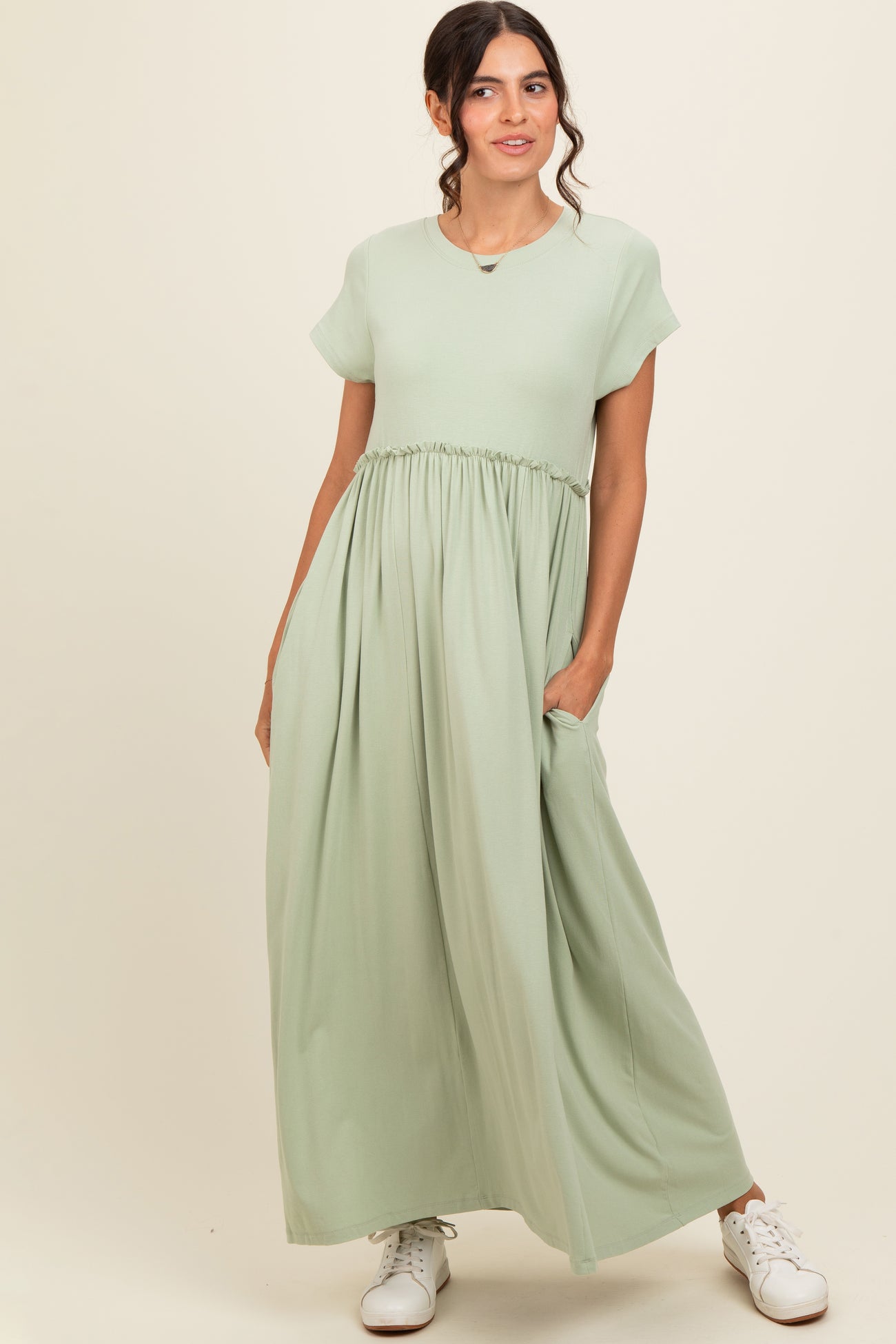 woman wearing a light green short sleeve maxi dress with a gathered waist and pockets, standing against a neutral background