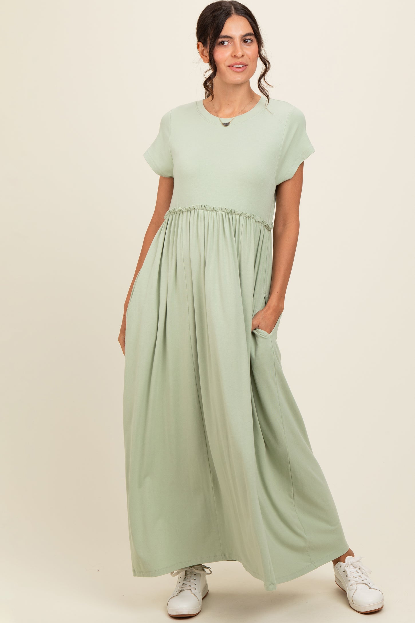 woman wearing a light green short sleeve maxi dress with a gathered waist and pockets, standing against a neutral background