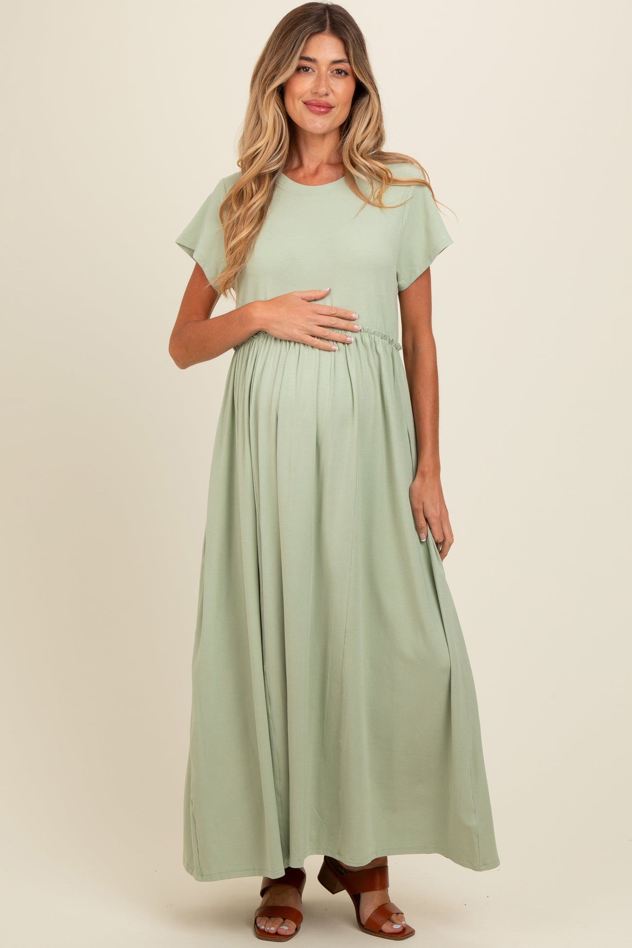 woman wearing a light green maxi maternity dress and holding her baby bump