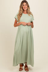 woman wearing a light green maternity maxi dress with short sleeves and a gathered waist, holding her baby bump