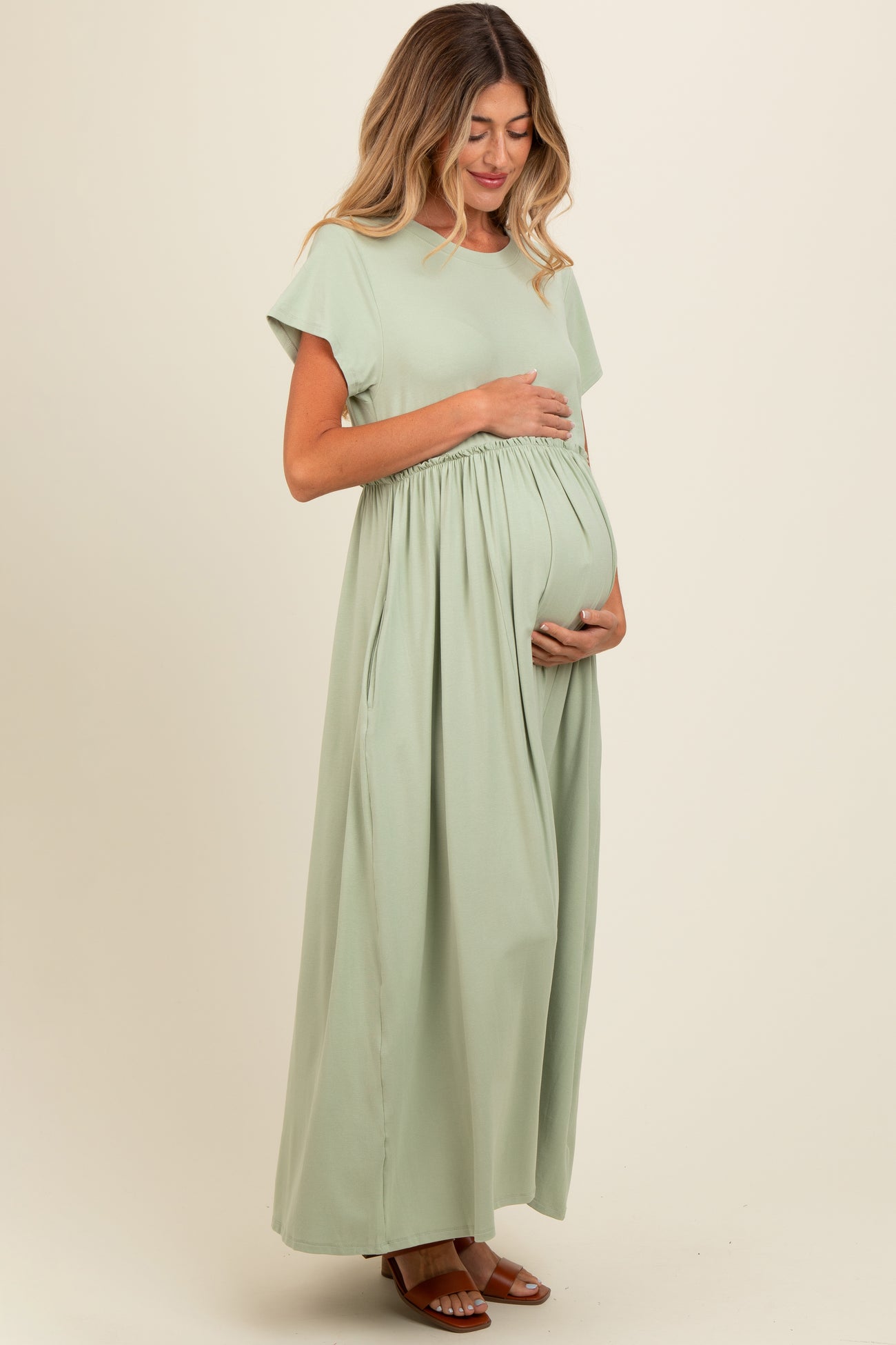 woman wearing a light green maternity maxi dress and holding her baby bump