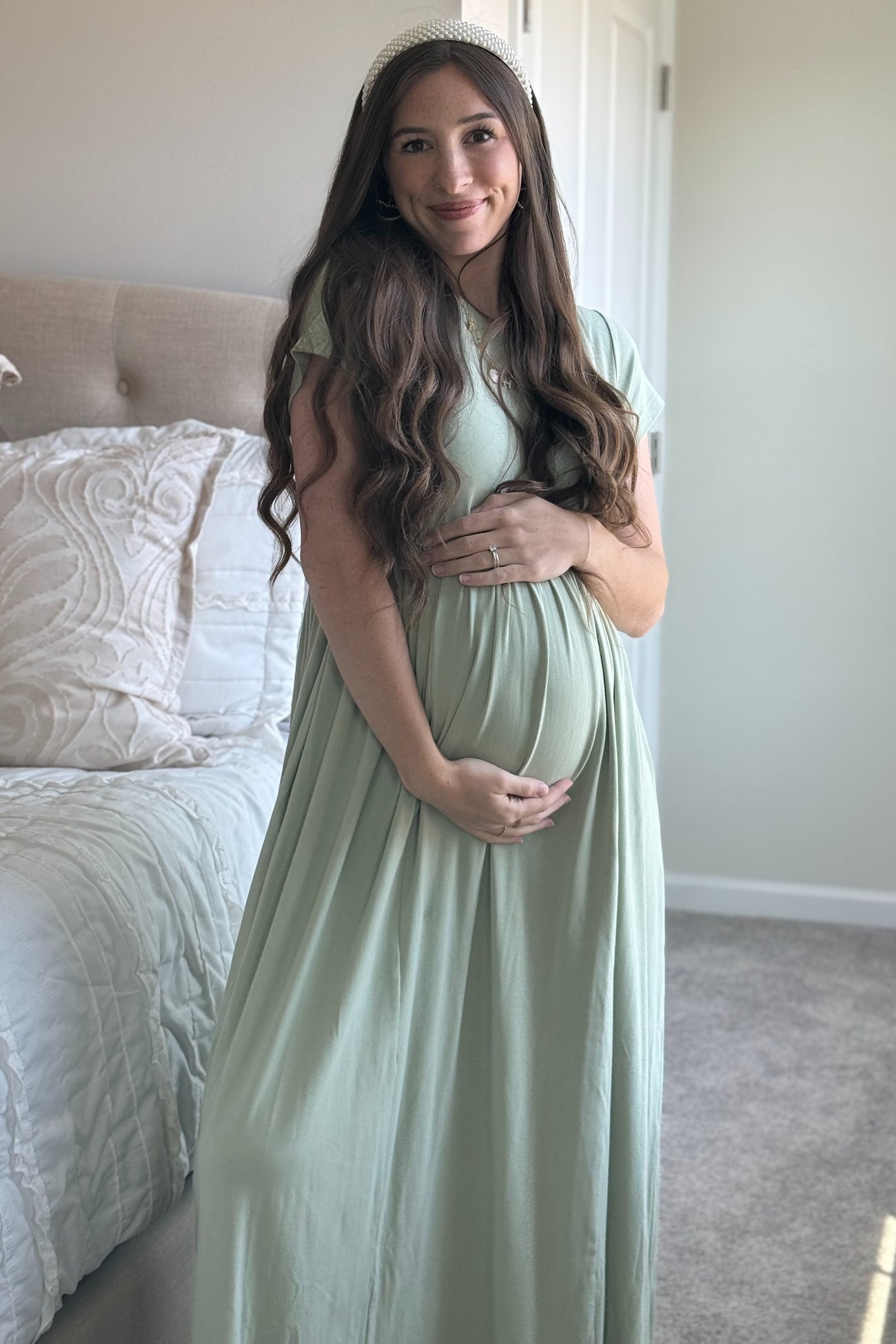 woman wearing a light green maternity dress and holding her baby bump
