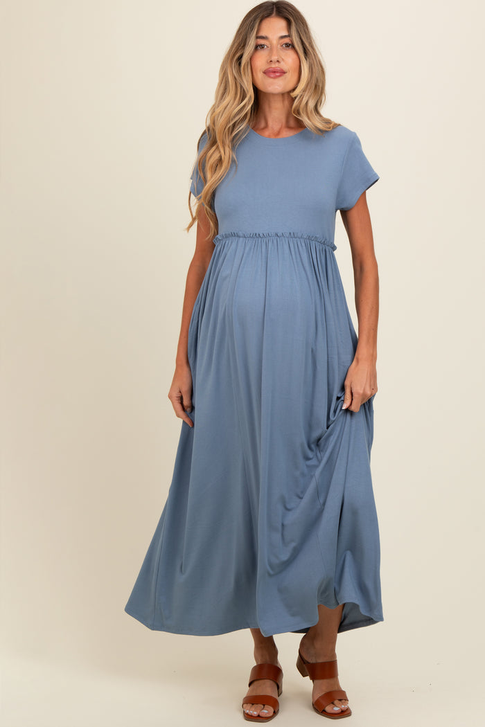 woman wearing a blue short sleeve maternity dress with a gathered waist and a flowing skirt, showing her baby bump