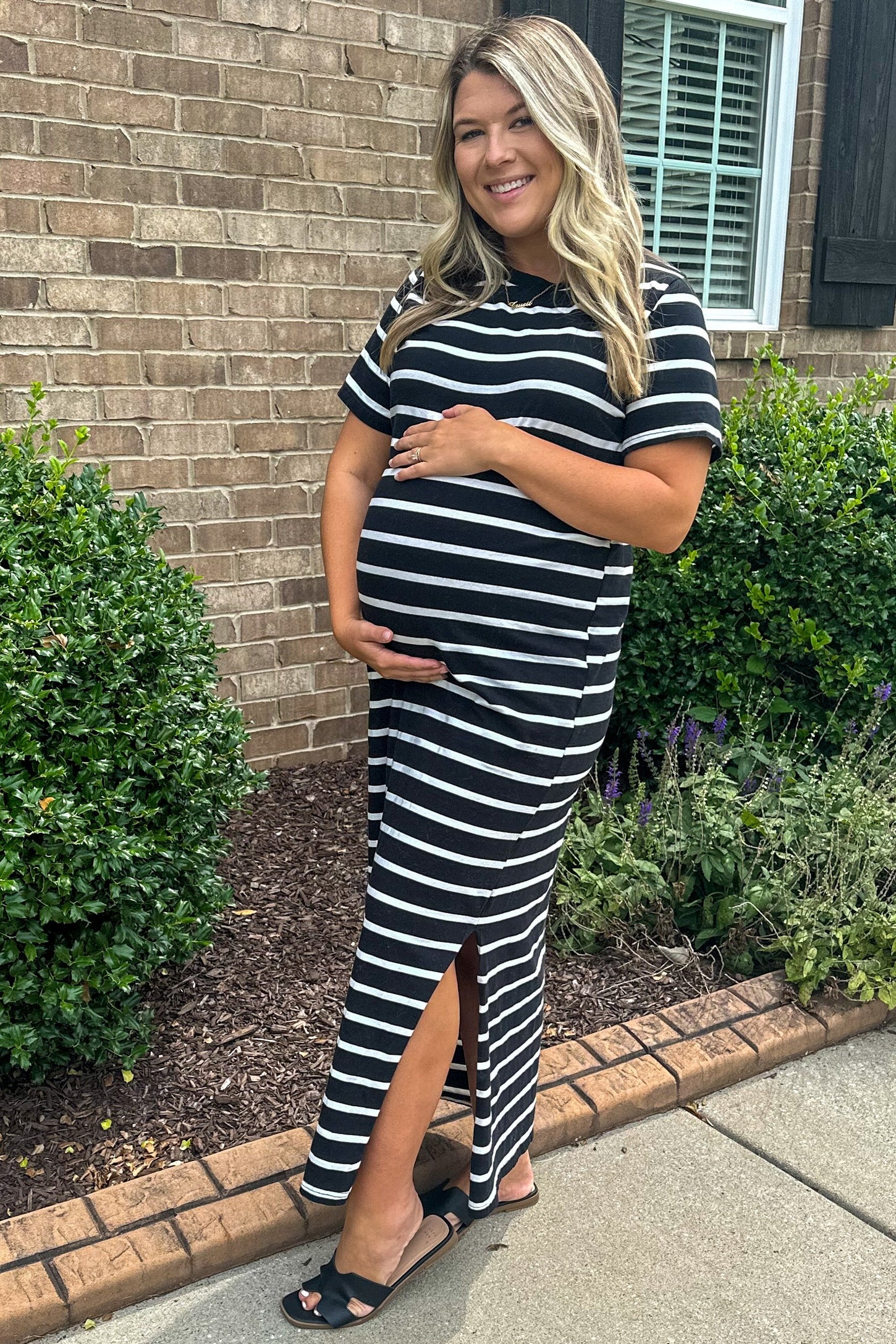 woman wearing a black and white striped maternity maxi dress with side slit and holding her baby bump