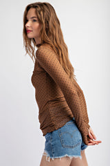 woman wearing a brown long sleeve polka dot top with a fitted silhouette and distressed denim shorts