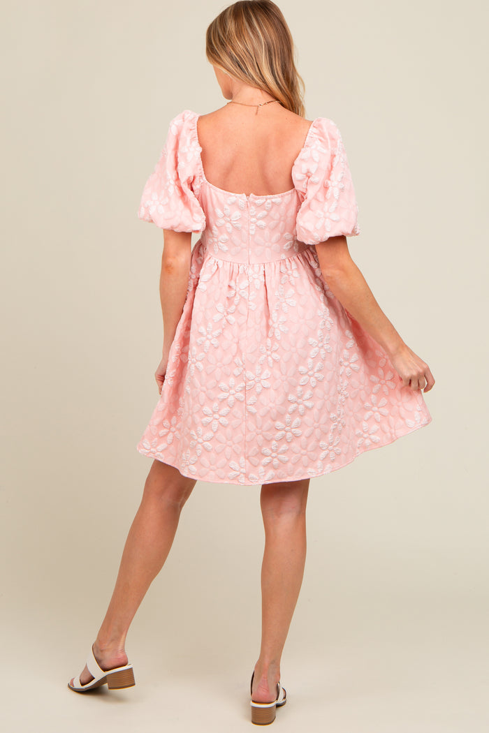 woman wearing a light pink maternity dress with puff sleeves and floral embroidery, showcasing a delicate a-line silhouette