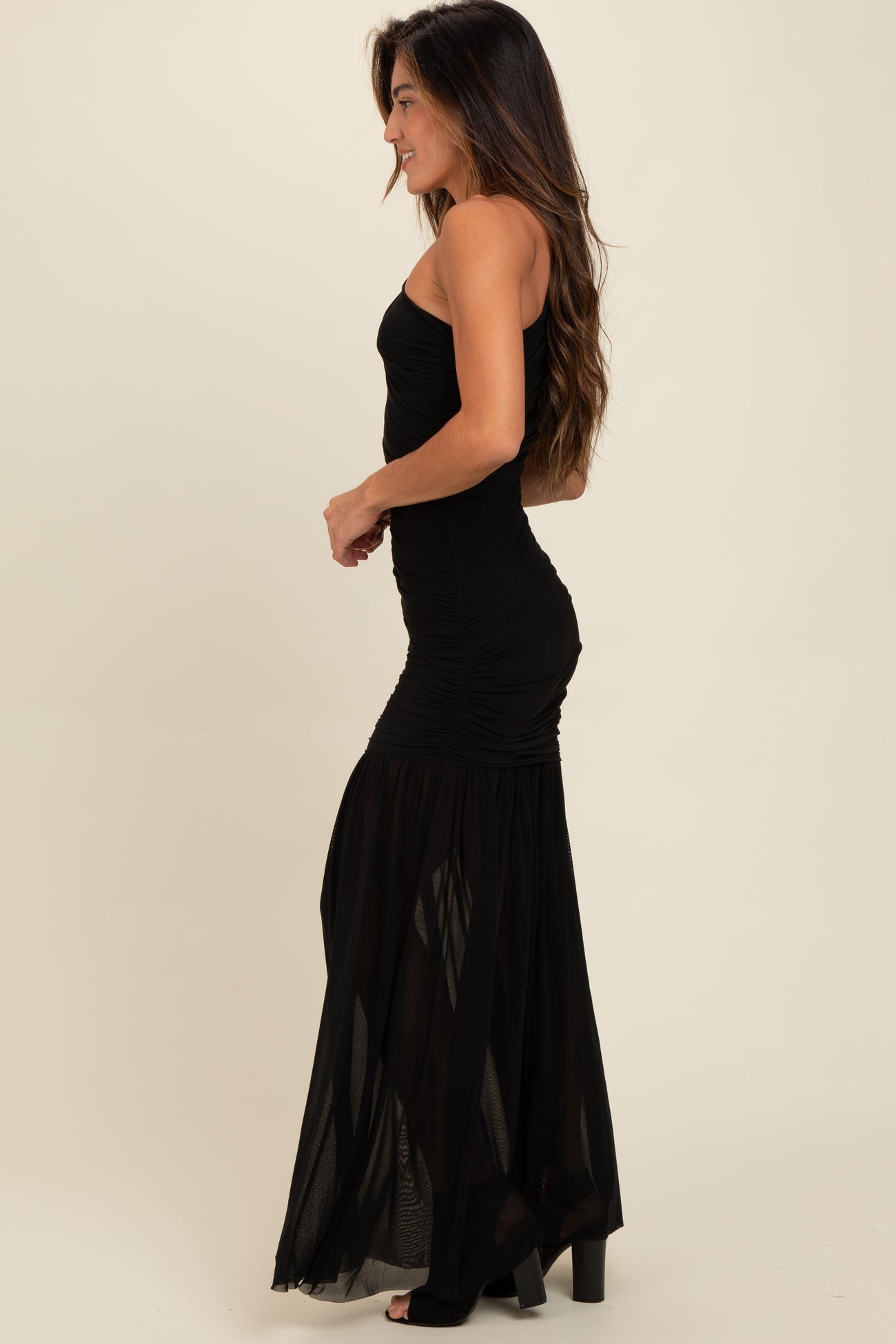 woman wearing a black strapless maxi dress with ruched detailing and a flowing skirt, shown from the side