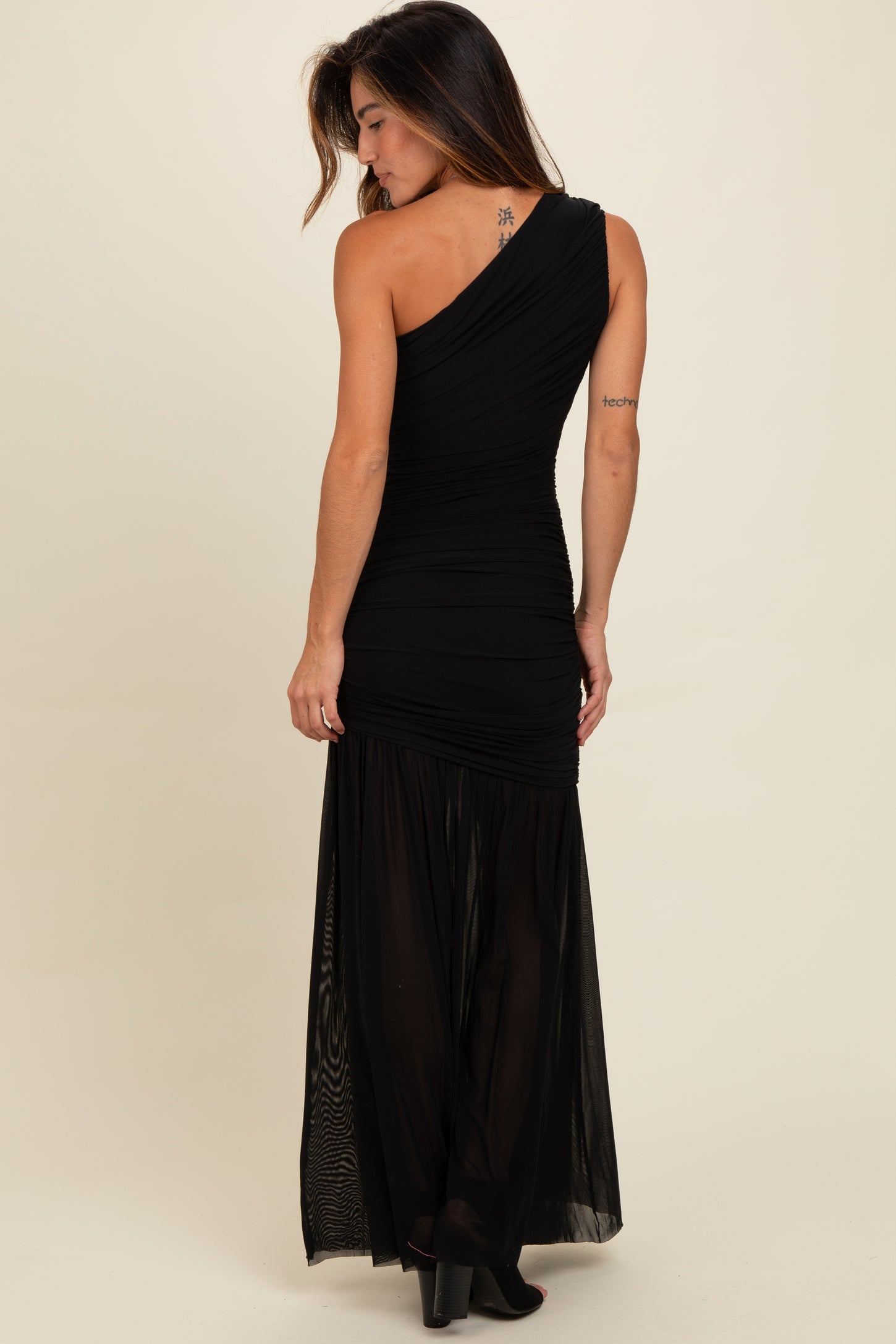 woman wearing a black one-shoulder evening gown with ruched details and a sheer maxi skirt
