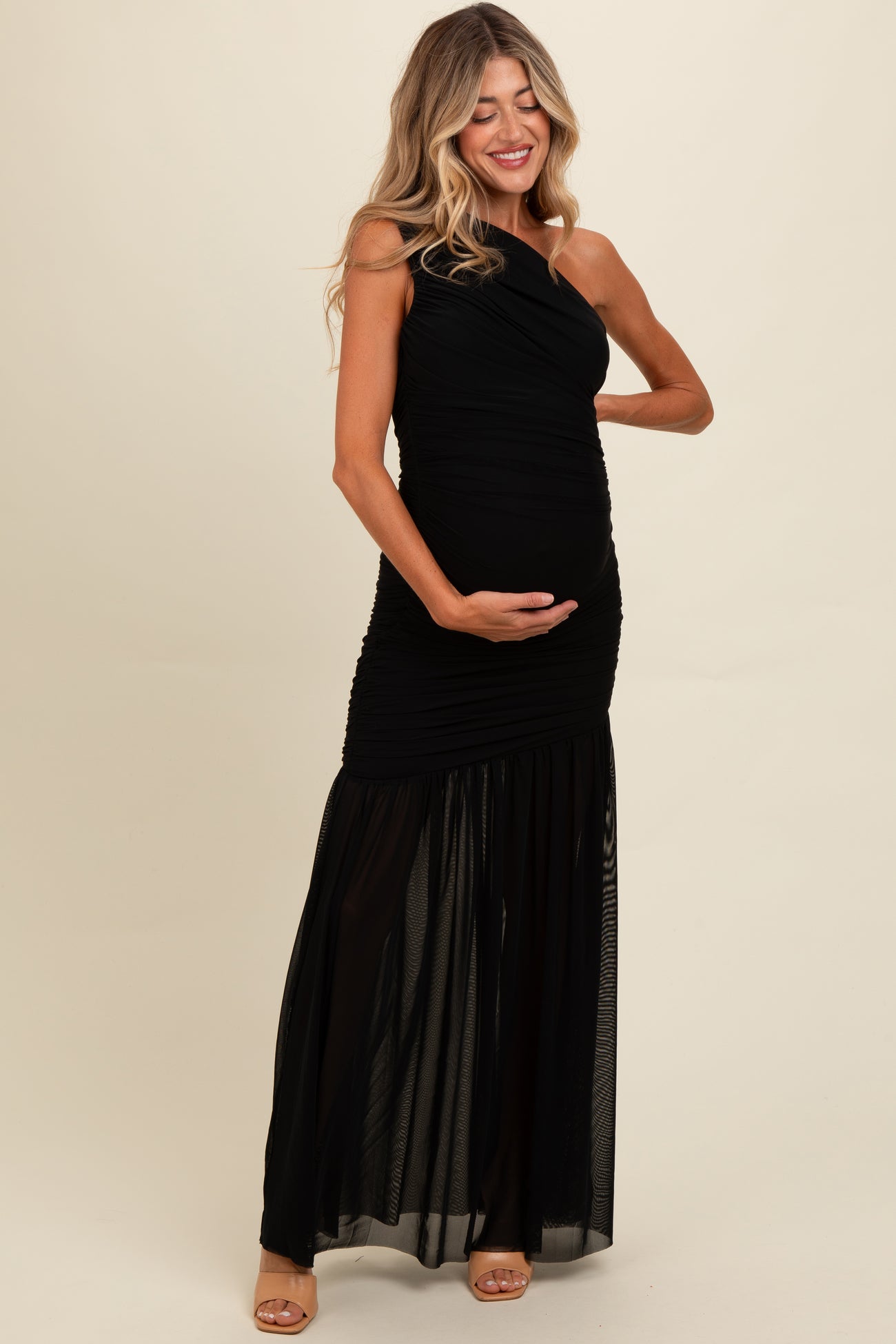 woman wearing a black one-shoulder maternity gown with a flowing skirt and holding her baby bump