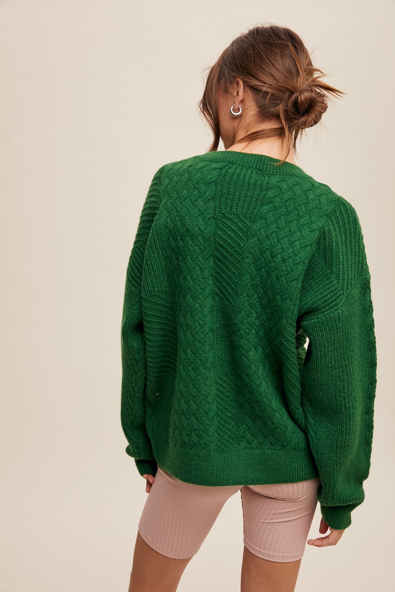 woman wearing a green cable knit oversized sweater with long sleeves, standing with her back to the camera