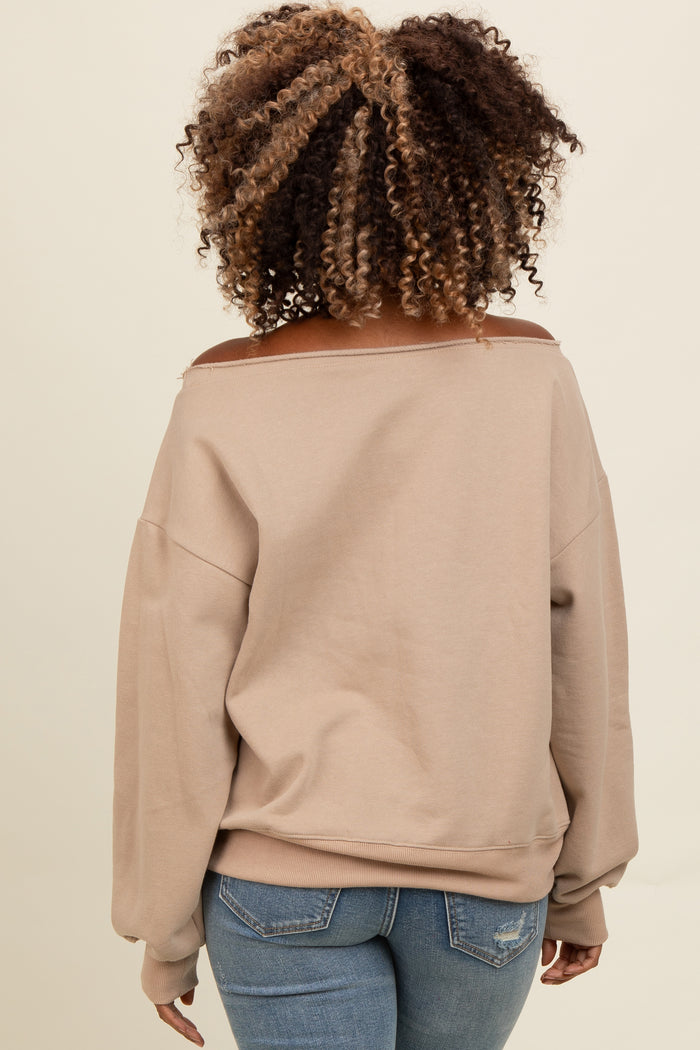 woman wearing a light brown off-the-shoulder sweatshirt with long sleeves and distressed back details, paired with blue jeans