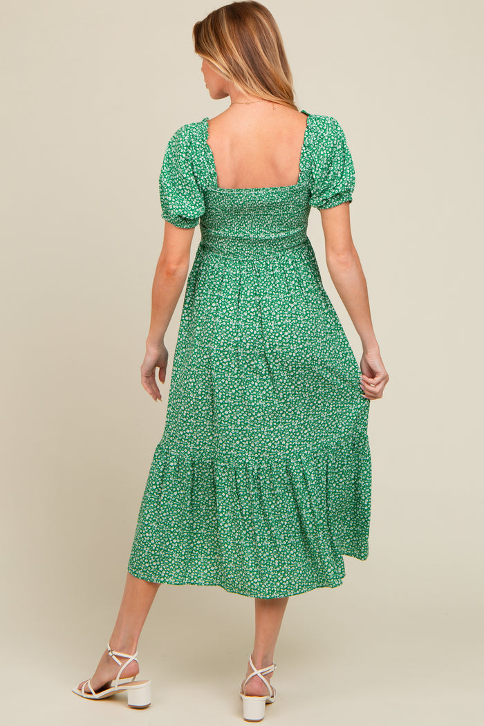 woman wearing a green floral maternity dress with puff sleeves and a tiered skirt, showing her baby bump from the back