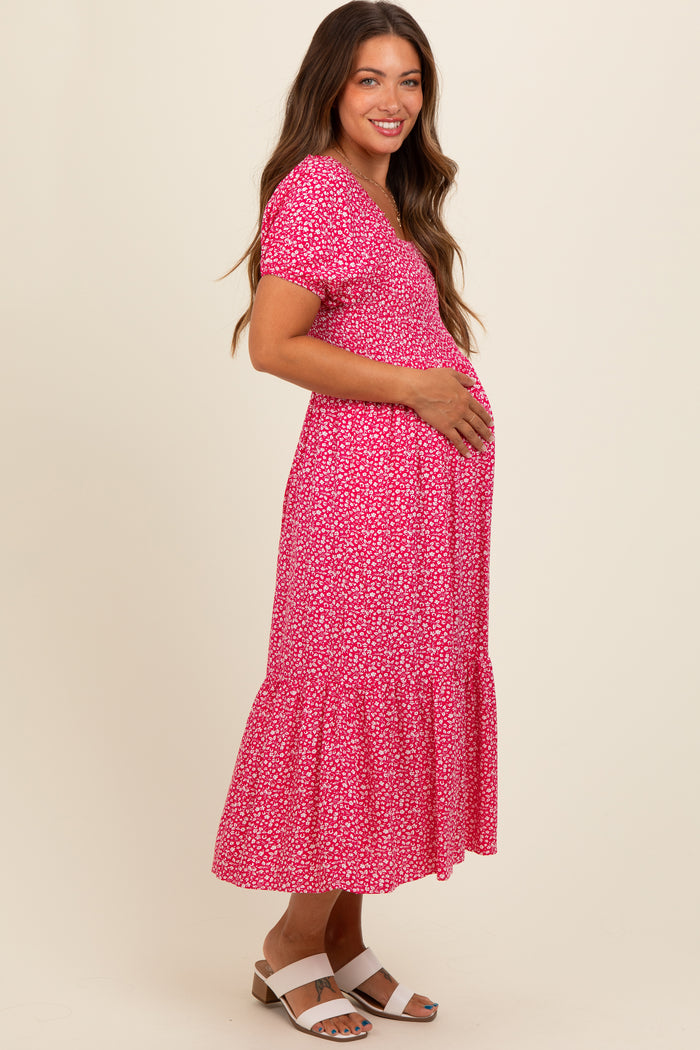 woman wearing a pink floral maternity dress with short sleeves and a tiered hem, holding her baby bump