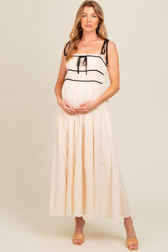 woman wearing a cream maternity maxi dress with black straps and holding her baby bump