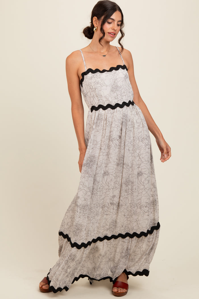 woman wearing a floral print maxi dress with black trim and spaghetti straps, posed with one hand on her hip