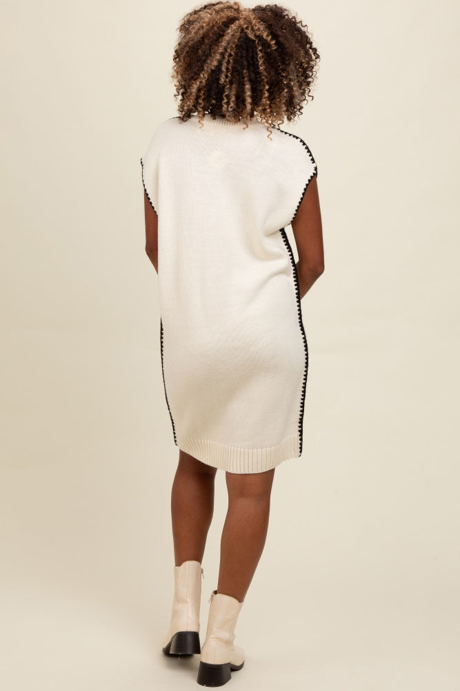 woman wearing a cream sleeveless knit sweater dress with black trims and ankle boots, shown from the back