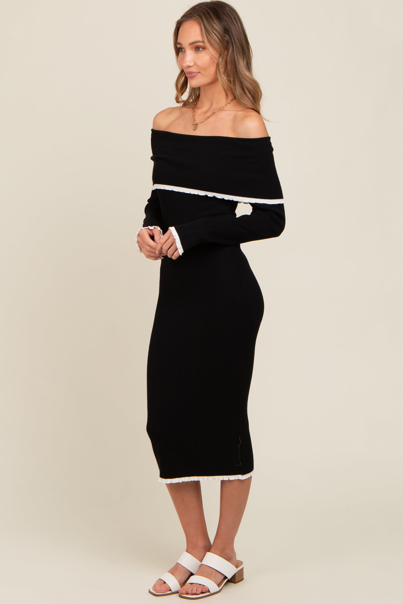 woman wearing a black ribbed off-the-shoulder midi dress with white trim and white heeled sandals