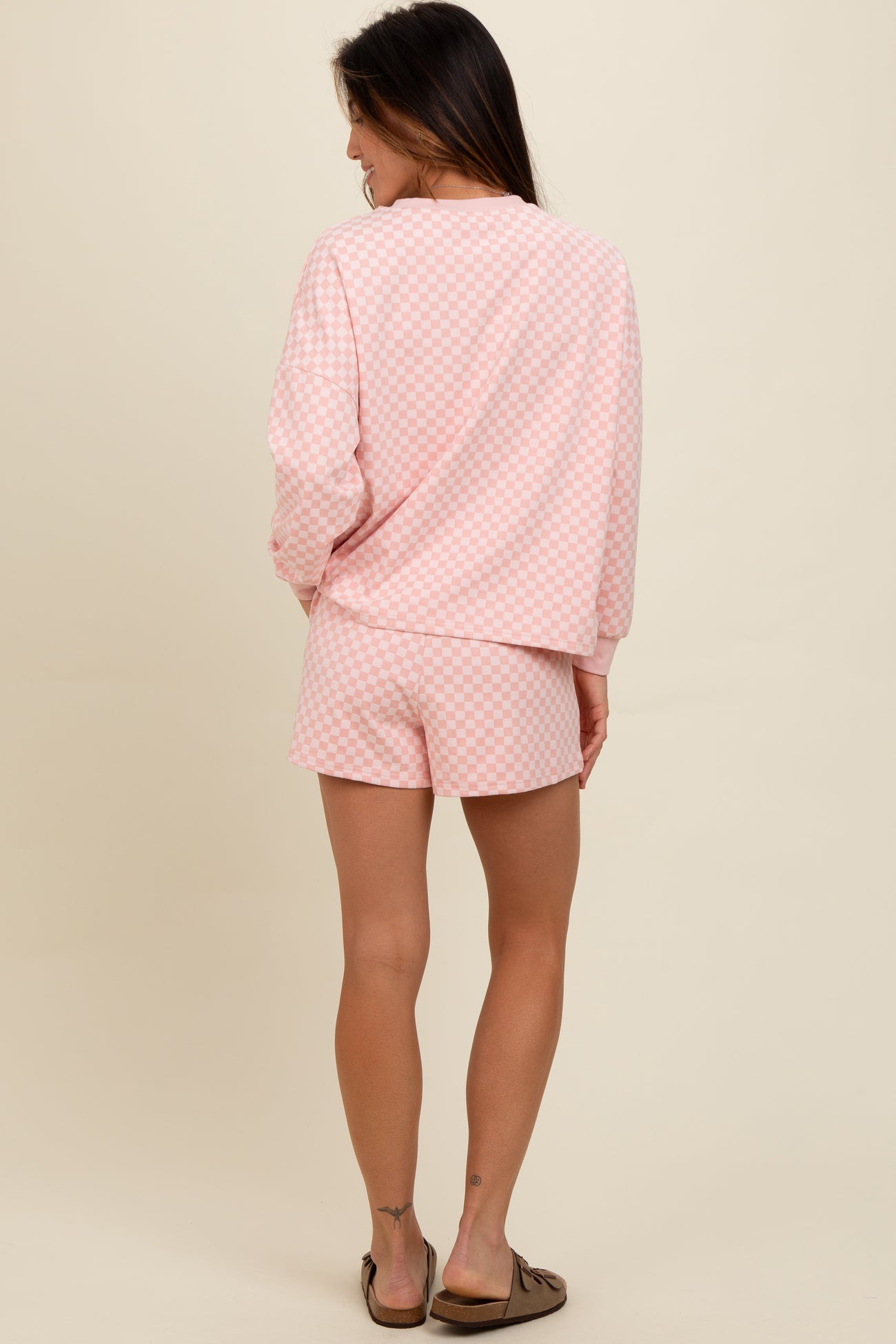 woman wearing a pink checkered loungewear set featuring a long sleeve top and shorts, viewed from the back