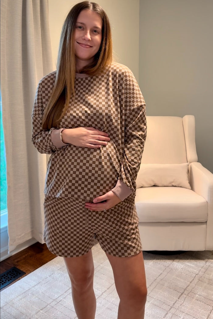 woman wearing a brown checkered maternity loungewear set with long sleeve top and shorts, showing her baby bump