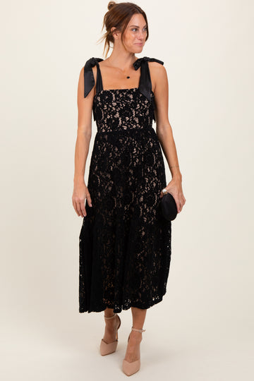 woman wearing a black lace midi dress with bow straps and holding a small black clutch