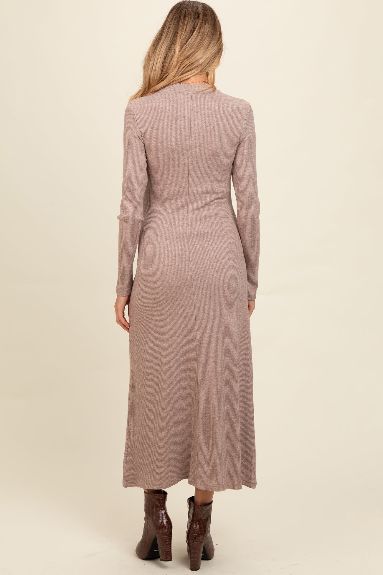 woman wearing a mauve long sleeve ribbed maternity dress, view from the back, with a fitted silhouette and ankle boots