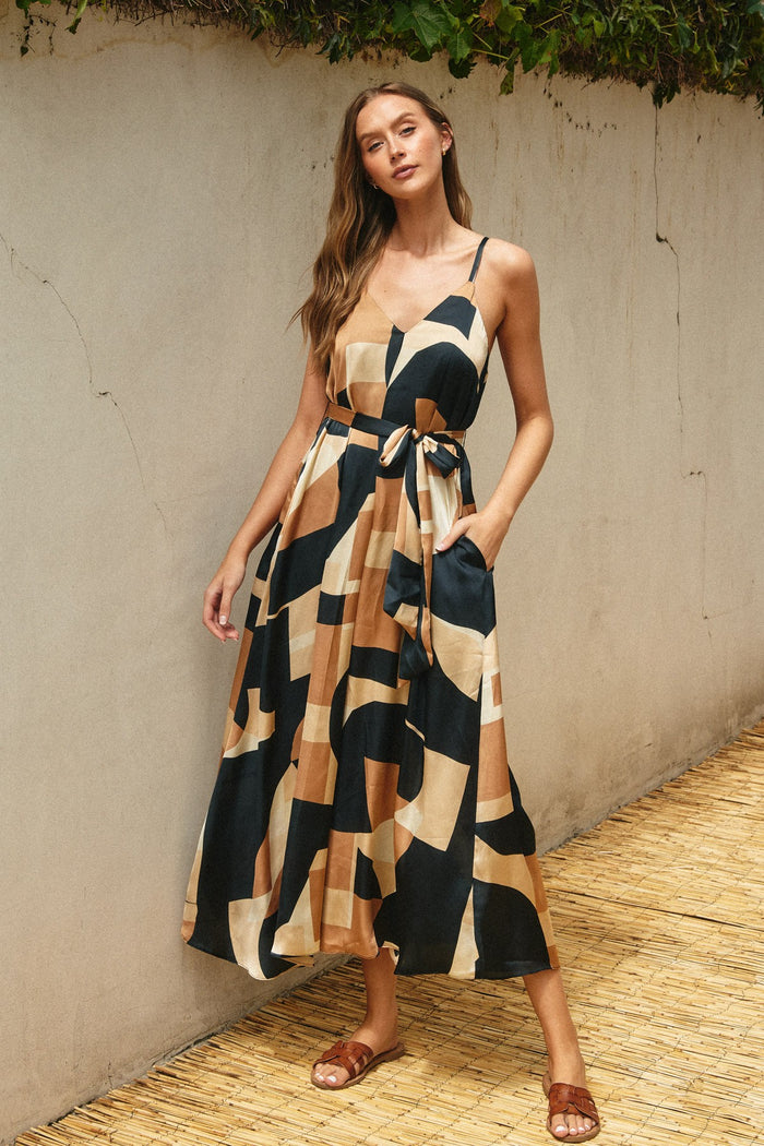 woman wearing a patterned maxi dress with spaghetti straps and pockets, featuring a tie waist detail