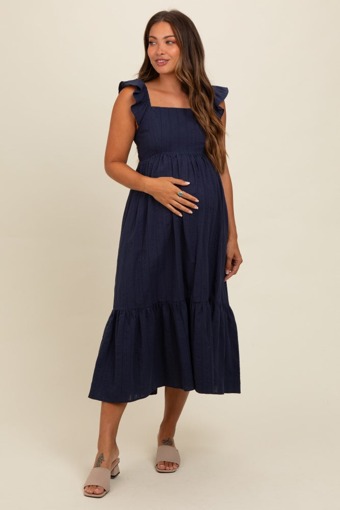 woman wearing a navy blue maternity dress with ruffle sleeves and a tiered skirt, showing her baby bump