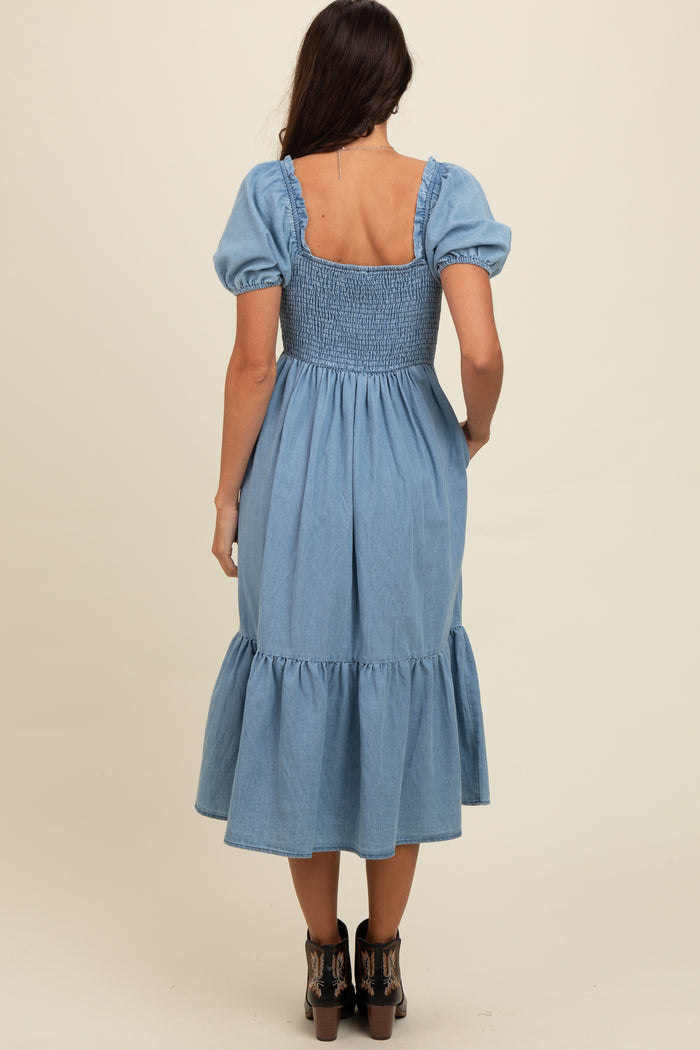 woman wearing a light blue denim dress with puffed sleeves and a smocked bodice, showcasing a tiered skirt