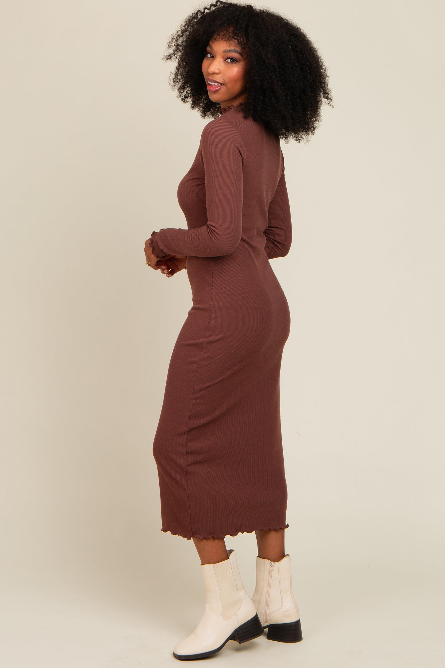 woman wearing a long brown ribbed dress with a scalloped hem and long sleeves, facing away from the camera