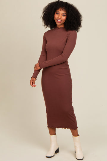 woman wearing a brown long sleeve ribbed midi dress with a fitted silhouette and a scalloped hem, paired with white ankle boots