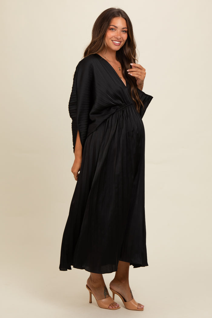 woman wearing a black pleated maternity dress with a deep V-neckline and a fitted waist, showcasing her baby bump