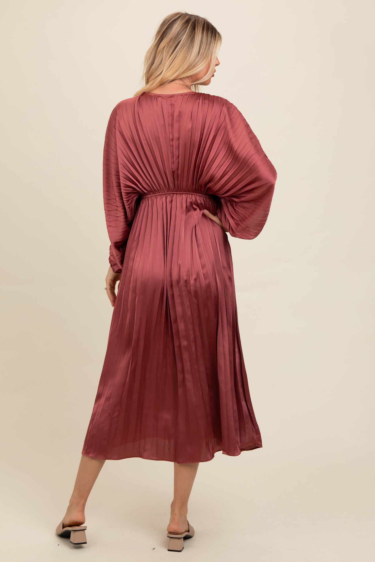 woman wearing a dusty rose pleated midi dress with a cinched waist and balloon sleeves, viewed from the back